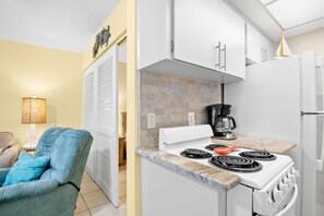 A compact kitchen with a stove, coffee maker, and a refrigerator.