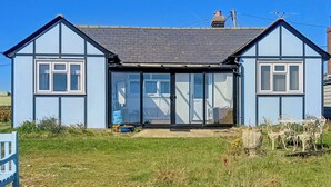 Une maison à deux étages avec une grande porte d’entrée en verre, un petit jardin et une façade bleue.