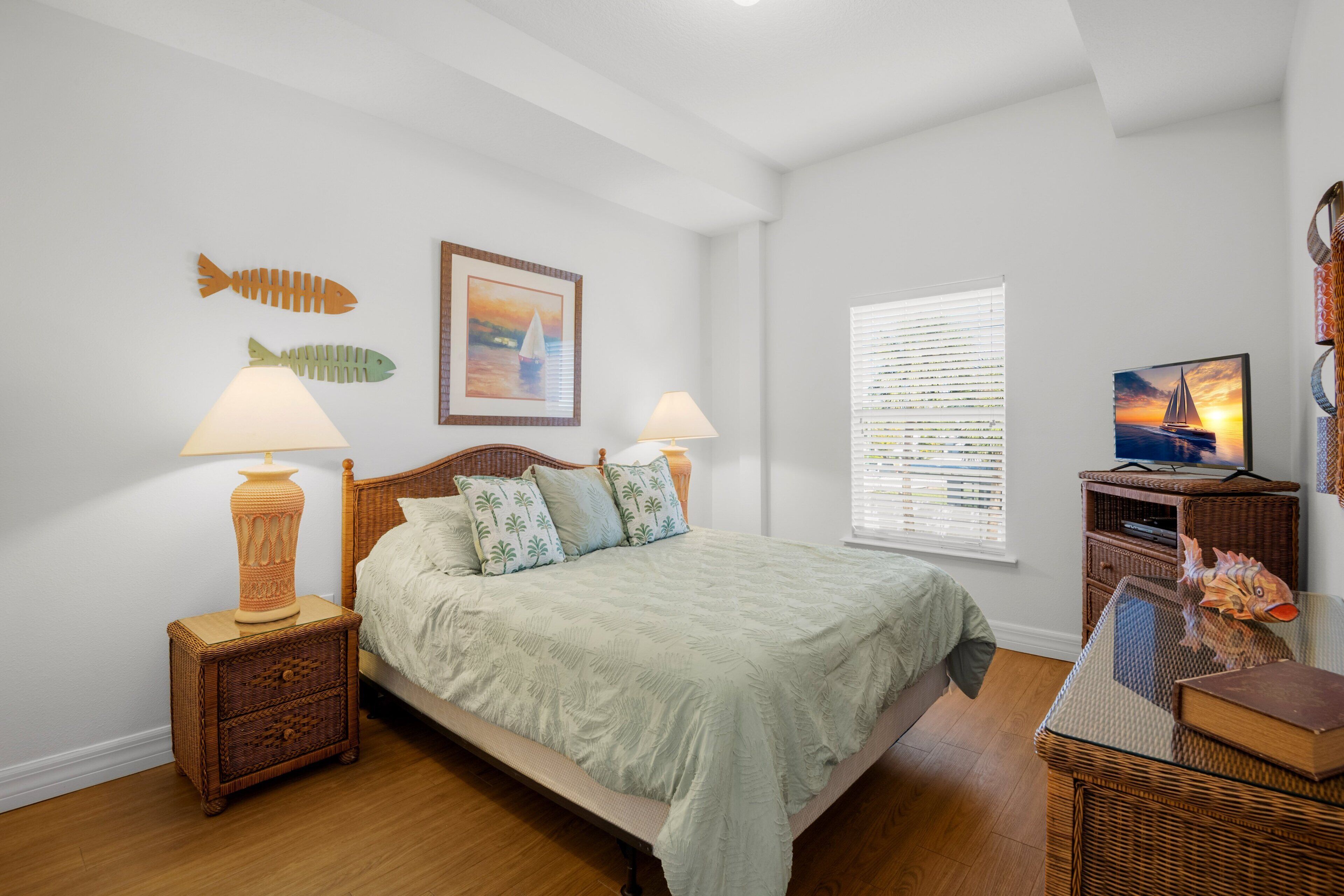 A bedroom with a bed, two nightstands, a television, and wall decorations including fish and a sailboat.