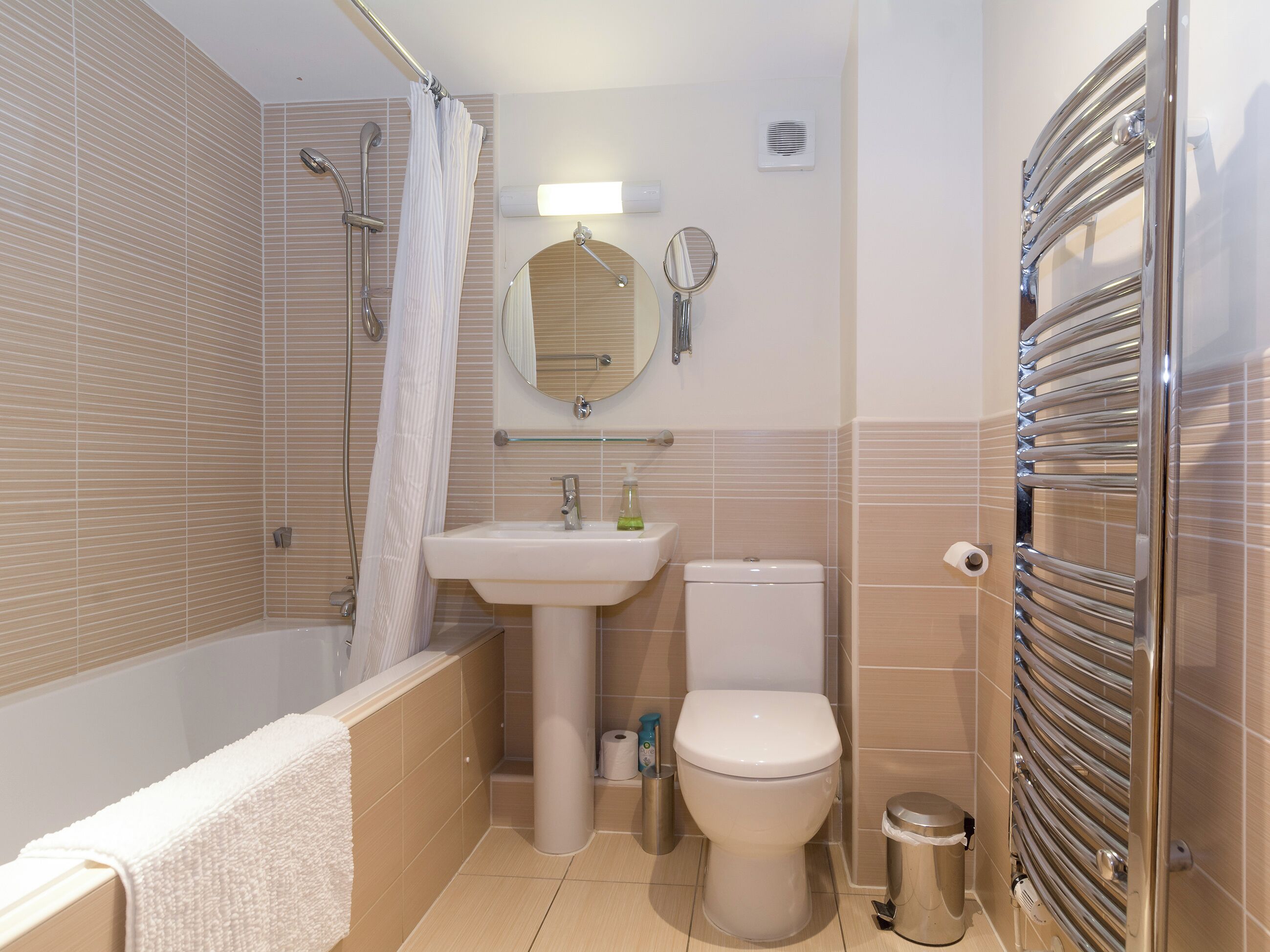 Un baño con bañera, lavamanos, inodoro y un perchero para toallas.