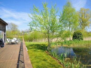 Una terraza de madera con mobiliario exterior, un estanque y árboles.