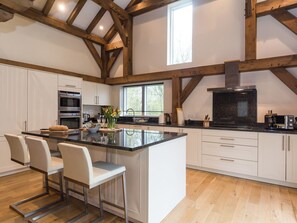 A modern kitchen with white cabinets, a central island with bar stools, a large stove, and a window with a view of trees.