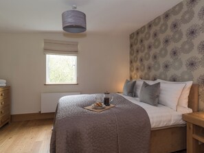 A bedroom with a bed, a window, a radiator, a wooden dresser, and a wall with a floral pattern.