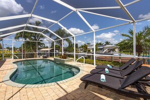 A covered outdoor swimming pool with lounge chairs and a view of a residential area. - Modern 4 Bed 3 Bath Waterfront Home with Quick Gulf Access&Heated Pool (Cape Coral)
