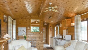 A cabin interior with two white sofas, a ceiling fan, wooden walls, a kitchen area, and a window with a view of greenery. - 2 bedroom accommodation in Churchstanton, near Honiton (Churchstanton, near Honiton)