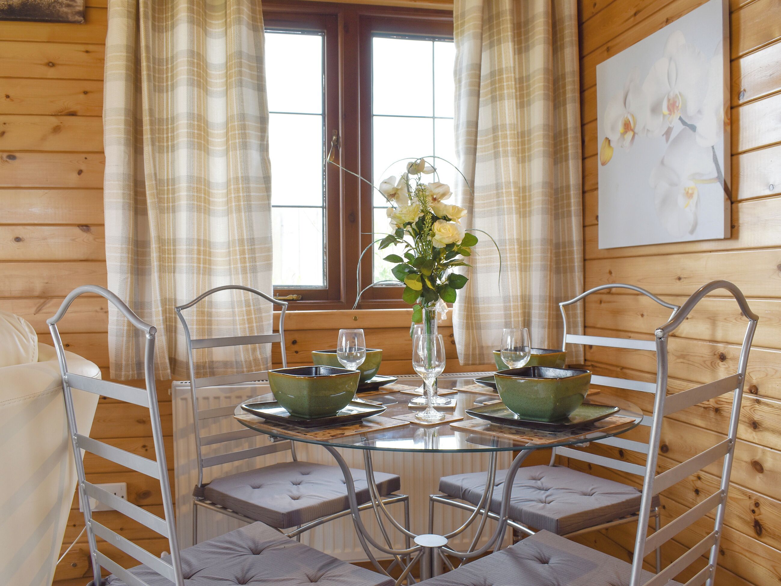 A dining area with a round glass table, metal chairs, and a vase of flowers.