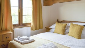 A bedroom with a bed, a nightstand, a window with curtains, and a radiator. - 2 bedroom accommodation in Churchstanton, near Honiton (Churchstanton, near Honiton)