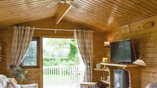 A cozy cabin interior with a wooden ceiling, a television, a sofa, a dining table, and a view of a garden through a glass door. - 2 bedroom accommodation in Churchstanton, near Honiton (Churchstanton, near Honiton)