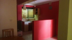 Una habitación con una pared roja, una ventana con barrotes, un radiador y una mesita pequeña.
