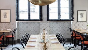 A dining area with a long table set for a meal, featuring a unique gold-colored ceiling sculpture, framed artwork on the walls, and a view of the outdoors through large windows. - Hotel de l'Abbaye (Lyon)