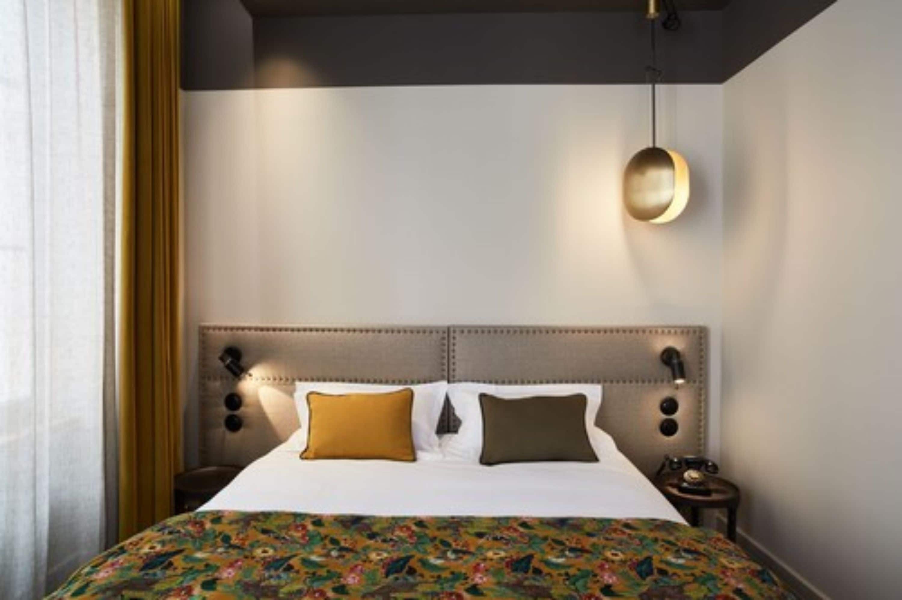 Une chambre d’hôtel avec un grand lit, une tête de lit agrémentée de lampes murales et une couvre-lit à motifs.