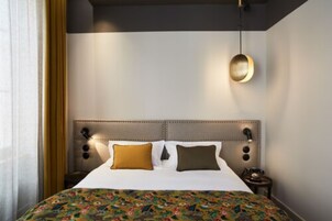 Camera d'albergo con un letto grande, una testiera con luci a parete e una coperta a motivi.
