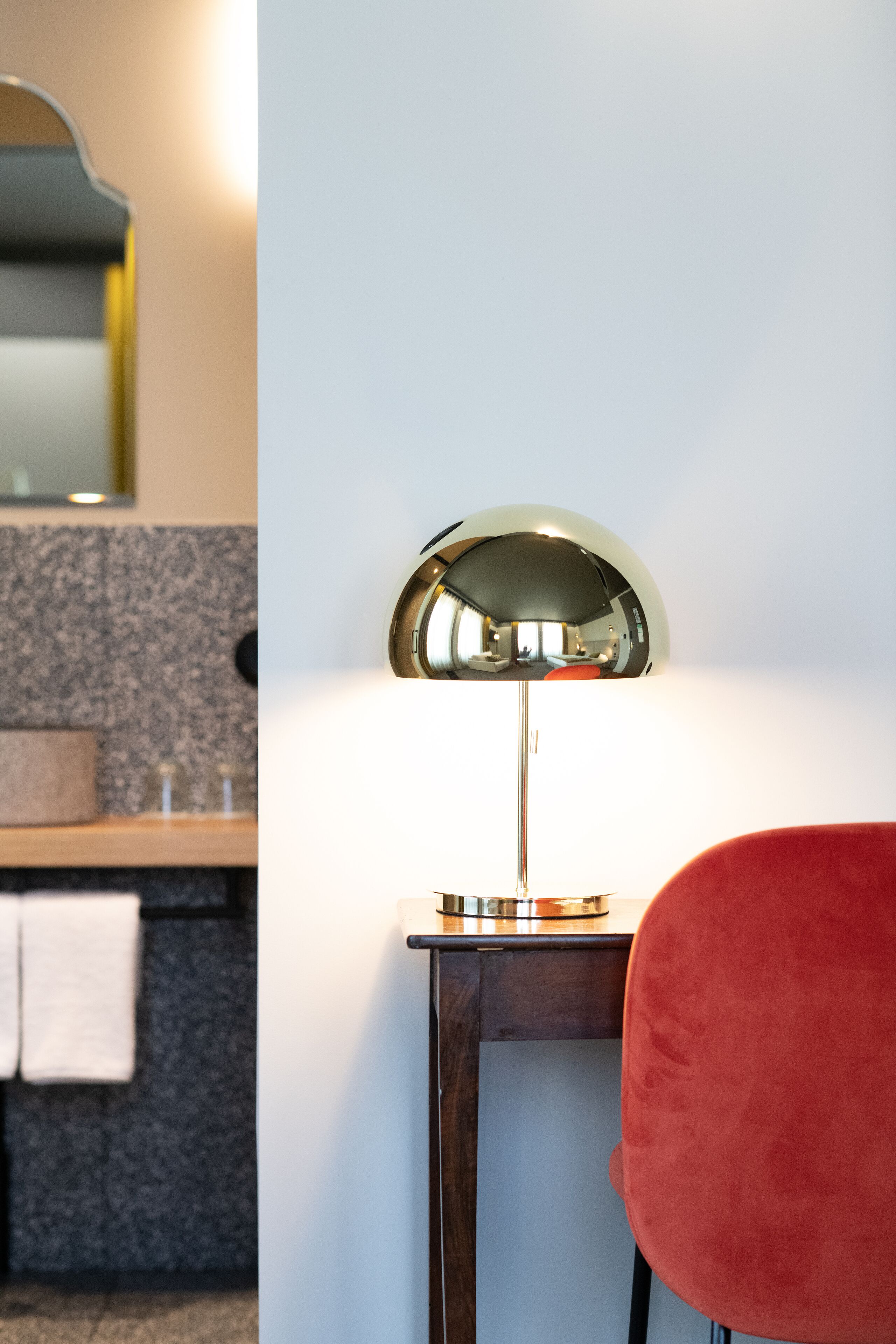 A modern bathroom with a round mirror, a wooden vanity, and a red chair.