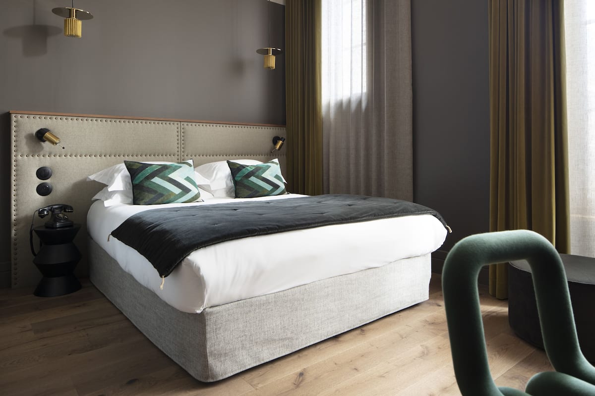A neatly made bed with a grey upholstered headboard, two pillows, and a black throw blanket.
