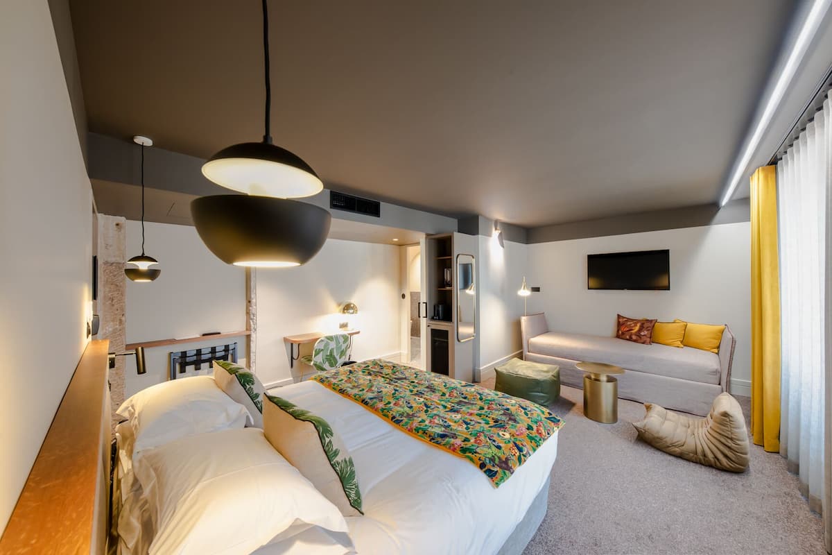 A modern hotel room with a large bed, a desk, a sofa, and a TV.