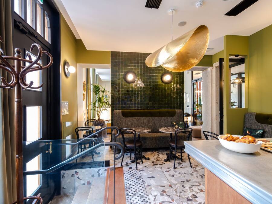 A modern restaurant interior with a green-tiled wall, a hanging light fixture, and a seating area with tables and chairs.