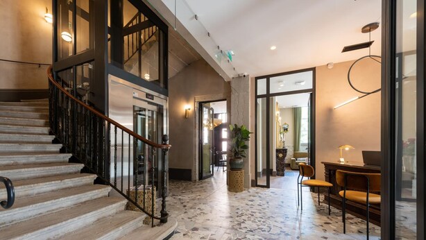 A spacious lobby with a terrazzo floor, a staircase with a wooden handrail, and a seating area with chairs and a table. - Hotel de l'Abbaye (Lyon)