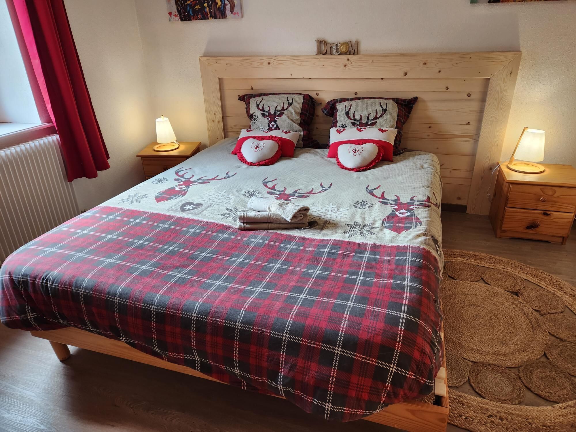 Una cama con una colcha escocesa, dos almohadas con diseños de renos y una mesita de noche con una lámpara.