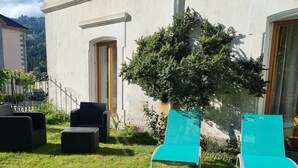Et grønt udendørsområde med to turkis liggestole, en sort sofa og et lille bord.