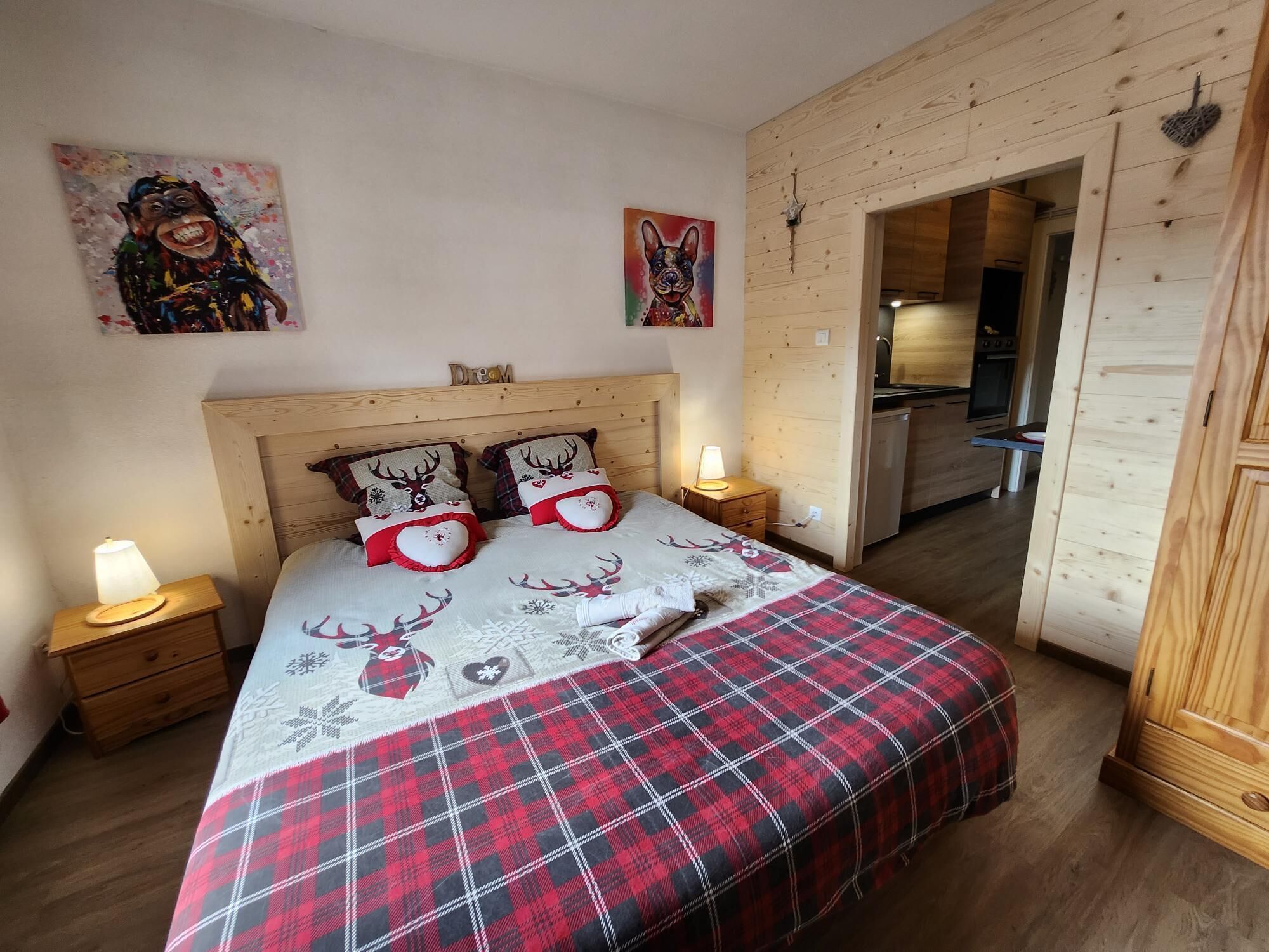 Ein Schlafzimmer mit einem Holz-Kopfteil, einem Bett mit rot-schwarz kariertem Bettbezug, zwei herzförmigen Kissen und einem Nachttisch mit einer Lampe.