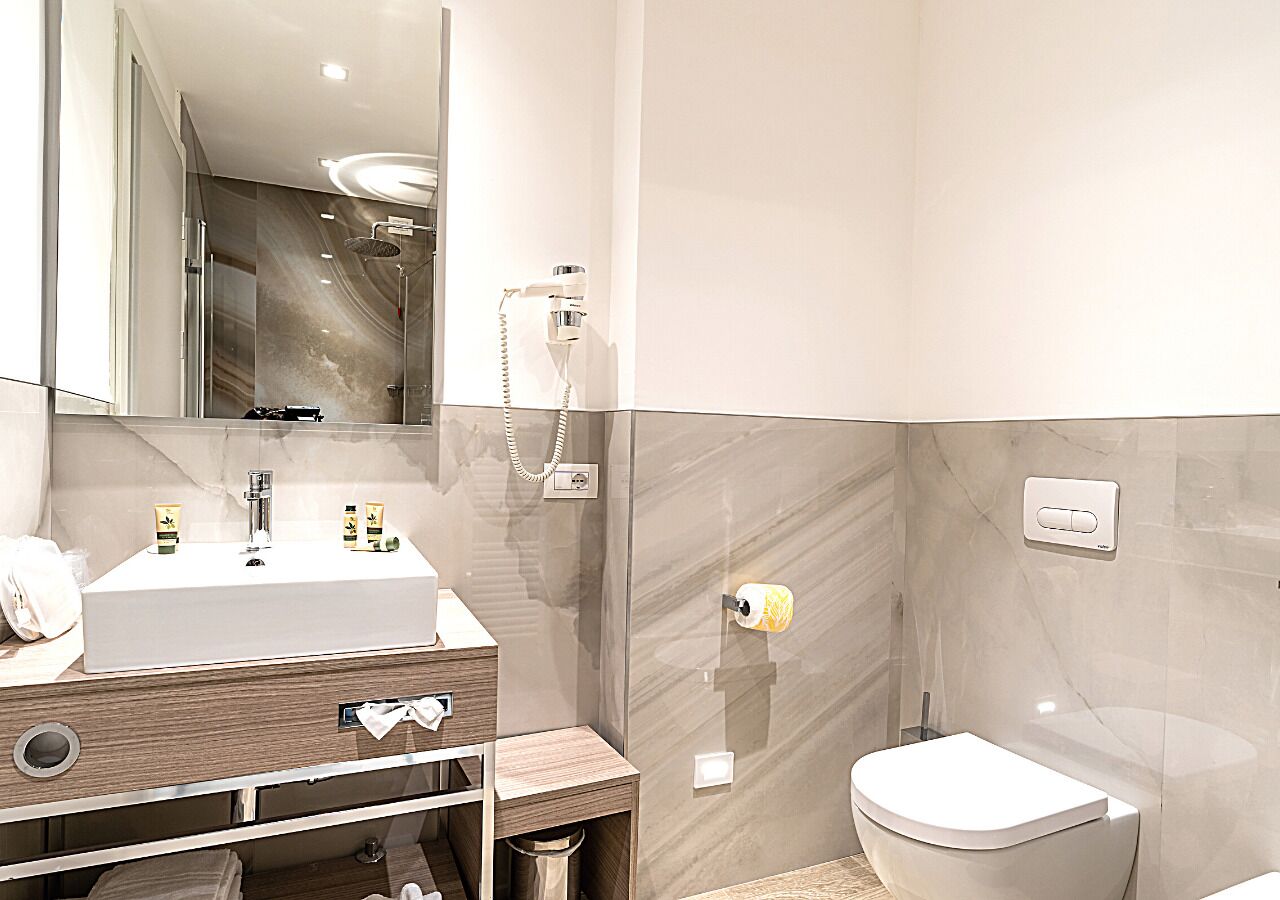 Ein modernes Badezimmer mit einem großen Spiegel, einem weißen Waschbecken und einer Toilette.