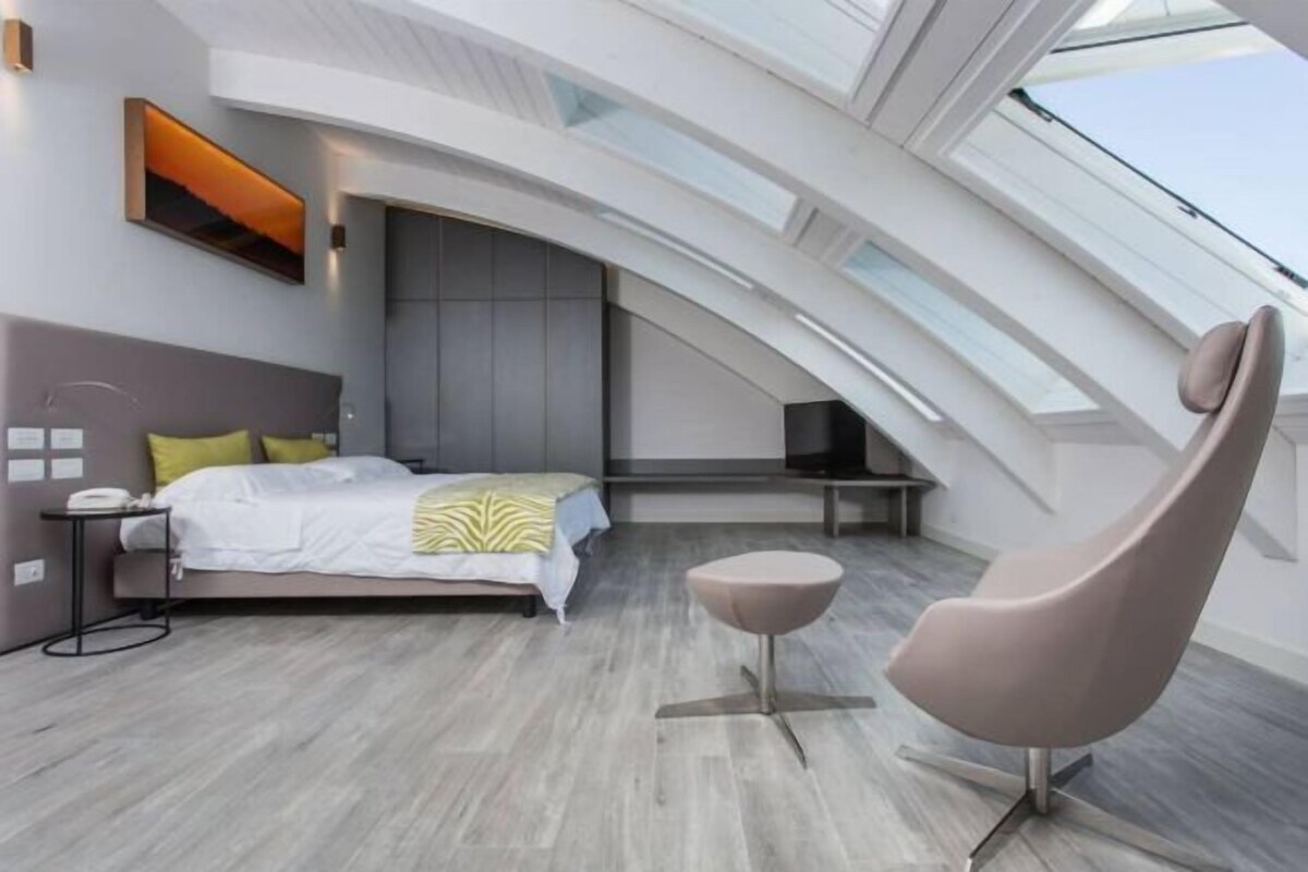 A modern bedroom with a skylight, a bed with a headboard, a bedside table, and a chair.