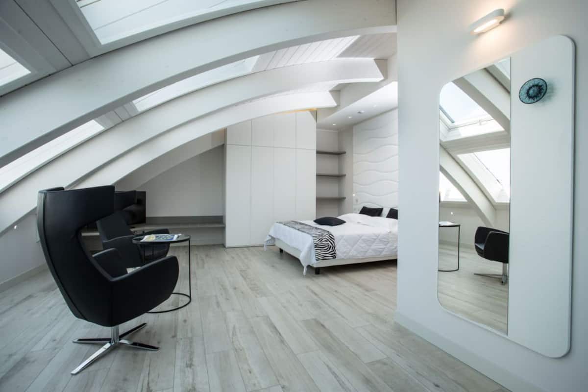 Een moderne slaapkamer met dakraam, een bed, een stoel en een grote spiegel.