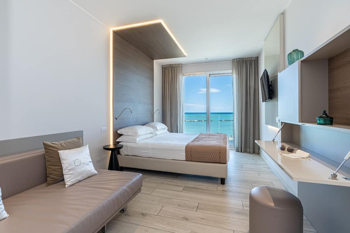 Een moderne hotelkamer met een bed, een bank, een bureau en uitzicht op zee.