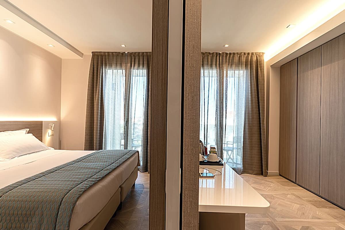 Een moderne hotelkamer met een groot bed, een bureau en uitzicht op de stad door grote ramen.