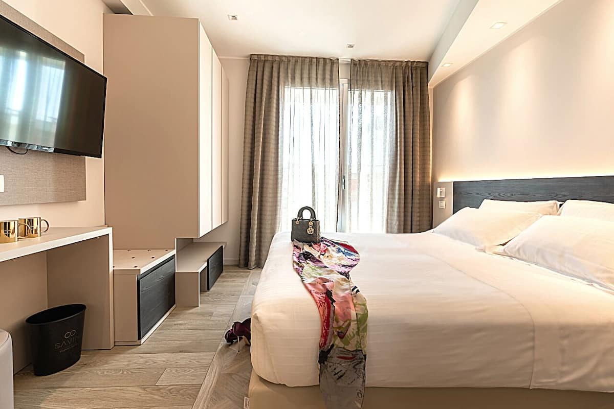 Hotelkamer met een bed, een aan de muur bevestigde televisie, een bureau met stoel en een raam met gordijnen.