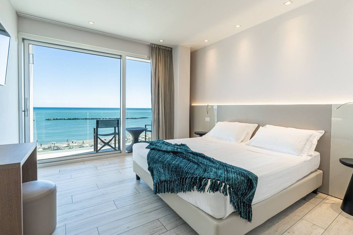Een moderne hotelkamer met een groot bed, een bureau en uitzicht op zee.