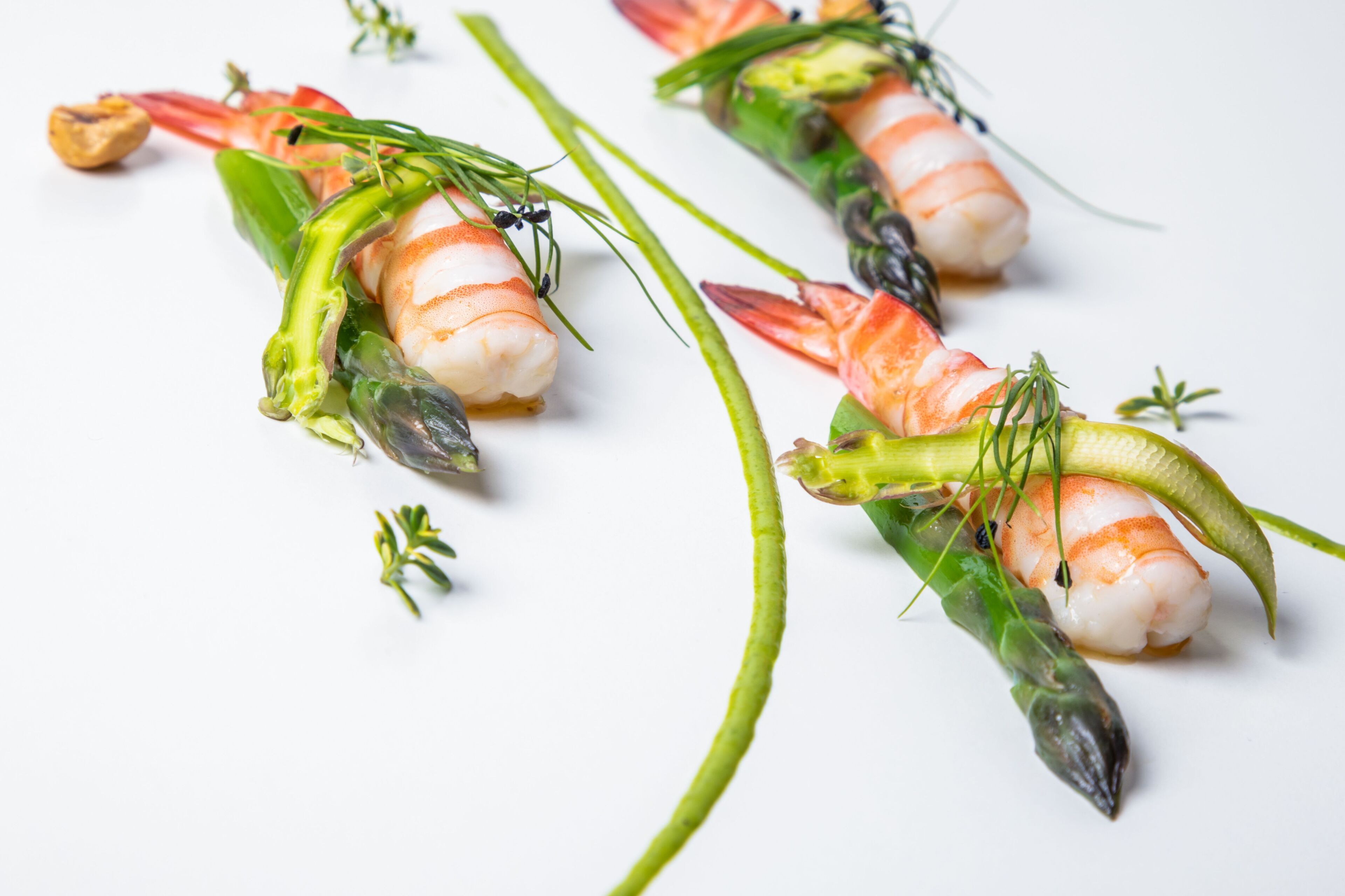 A plate of sushi with shrimp, asparagus, and garnishes.