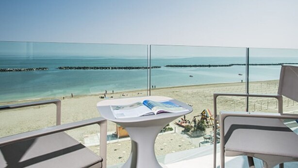 Ein Balkon mit Tisch und Stühlen mit Blick auf einen Strand und das Meer.
