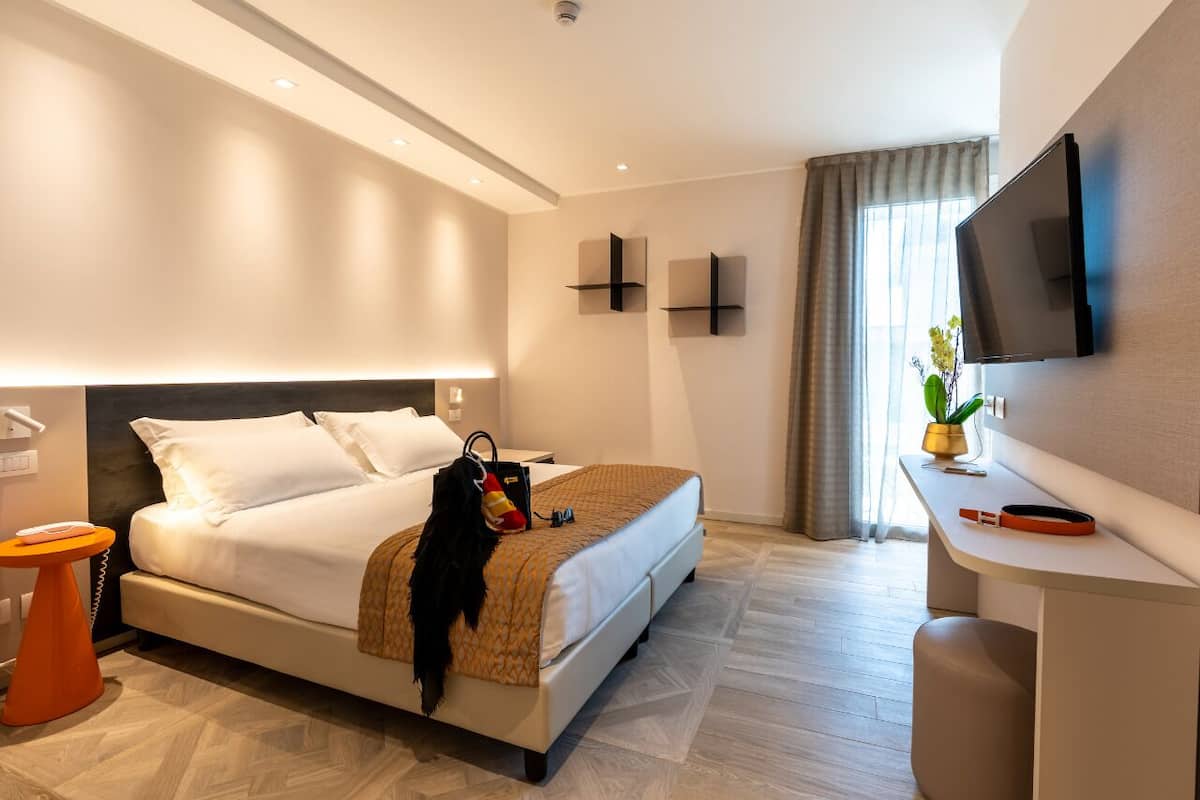Een moderne hotelkamer met een bed, nachtkastje, televisie en een bureau met stoel.