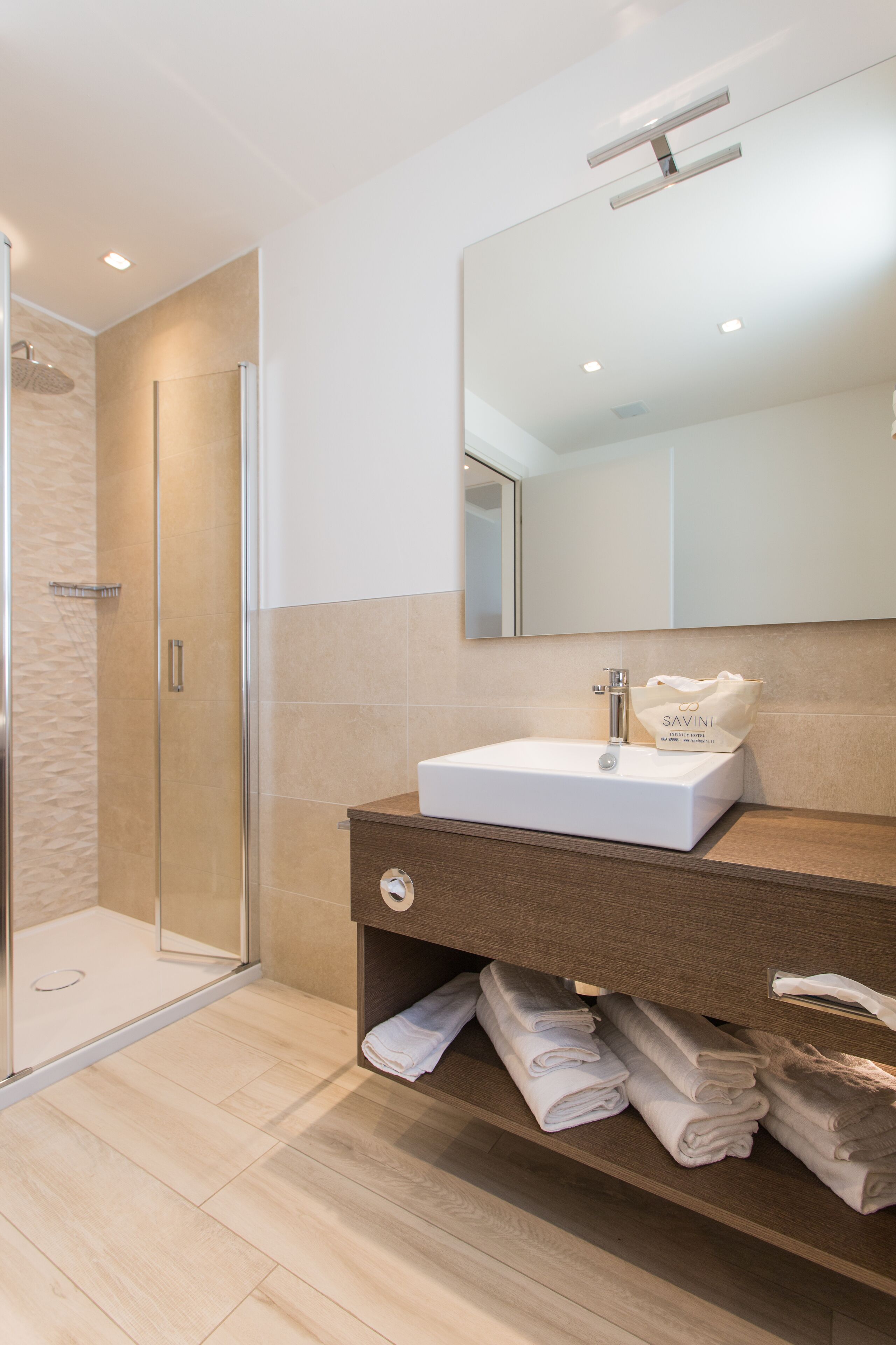 A modern bathroom with a glass shower enclosure, a white sink, a wooden vanity, and neatly folded towels.