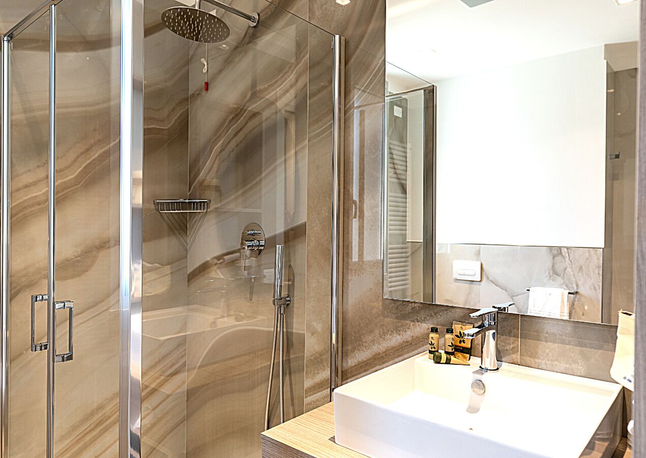A modern bathroom with a glass-enclosed shower, a large mirror, and a white sink with toiletries.