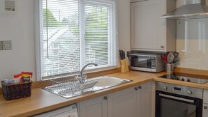 A compact kitchen with a dishwasher, oven, microwave, and a window with blinds. - 2 bedroom accommodation in Benllech (Benllech)