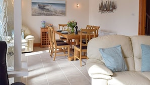 A dining area with a wooden table, chairs, and a painting of a boat on the wall. - 2 bedroom accommodation in Fishguard (Fishguard)