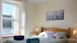 A bedroom with a bed, two bedside tables, a window with curtains, and a floral painting on the wall. - 2 bedroom accommodation in Fishguard (Fishguard)