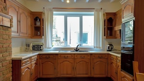 A kitchen with wooden cabinets, a built-in oven, and a window with curtains. - 2 bedroom accommodation in Fishguard (Fishguard)