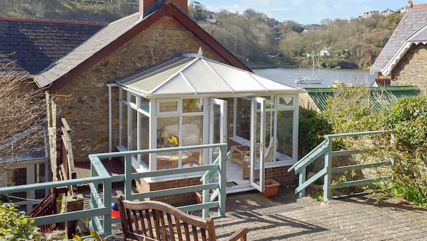 A traditional stone house with a conservatory, a wooden bench, and a view of a lake. - 2 bedroom accommodation in Fishguard (Fishguard)