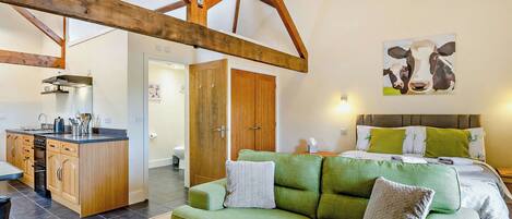 A cozy room with a green sofa, a bed with green and white bedding, a wooden ceiling, and a painting of cows on the wall.