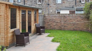 Eine Holzausfachung mit einer Glastür, die auf eine Terrasse mit Korbmöbeln führt.