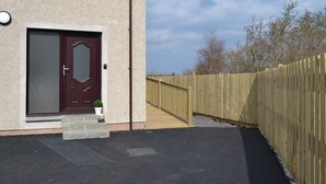 A building with a wooden fence, a door, and a small step leading to the entrance. - 2 bedroom accommodation in Oban (Oban)