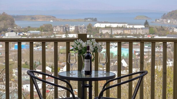 A balcony with a table and chairs overlooking a coastal town and body of water. - 2 bedroom accommodation in Oban (Oban)