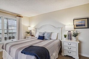 A bedroom with a large bed, bedside tables, a window with curtains, and a framed picture on the wall.