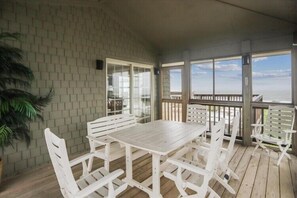 A covered outdoor patio with a wooden table and chairs, a potted plant, and a view of the ocean. - Fabulous Find - Spendlove Oceanfront (Duck)
