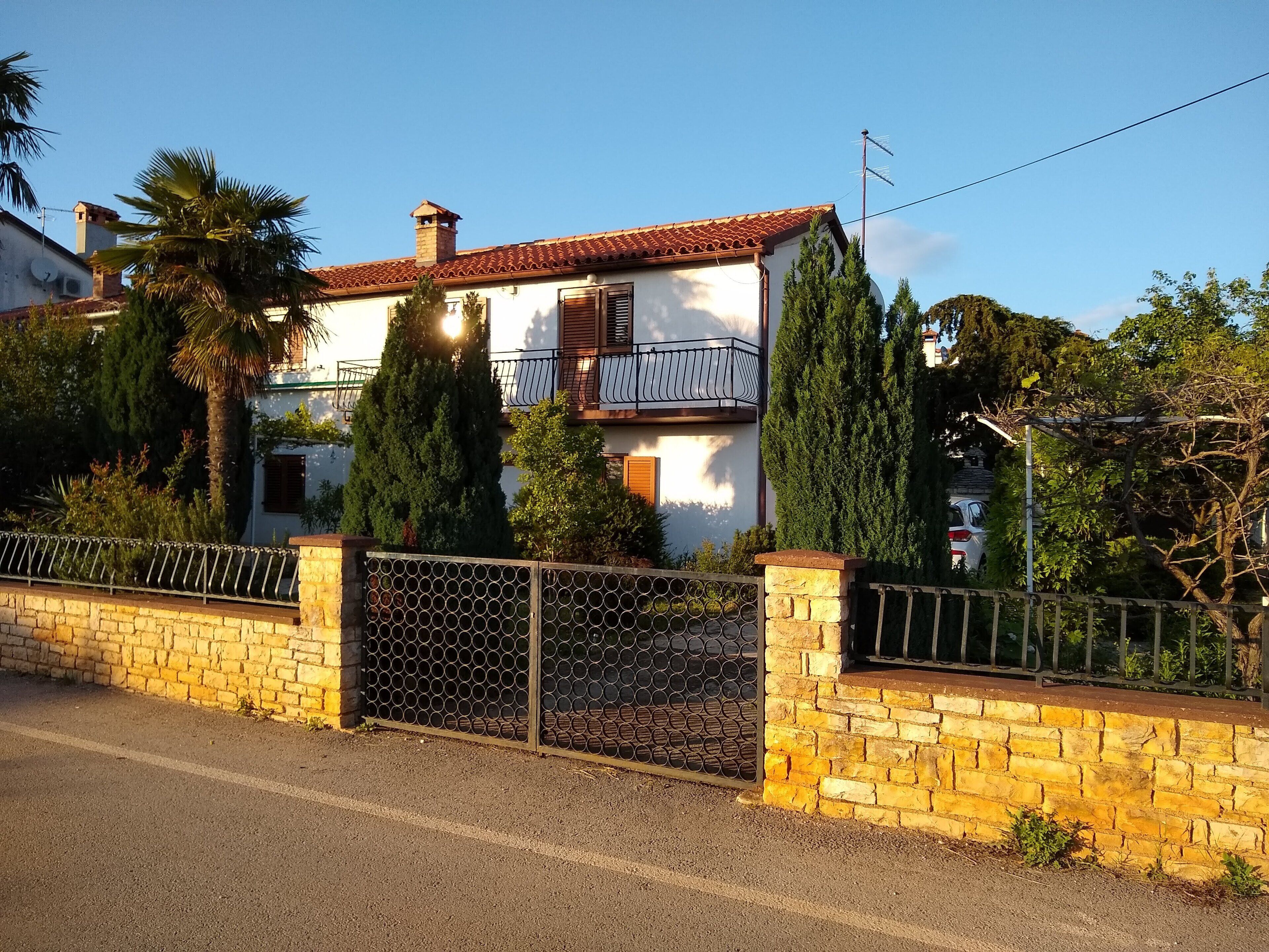A two-story house with a tiled roof, a balcony, and a gated entrance.