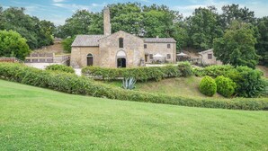 A stone building with a central chimney, surrounded by well-maintained hedges and a grassy foreground. - Anticheterme / Trilocale (Sorano GR)