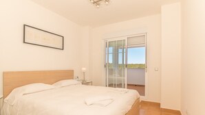A bedroom with a bed, a nightstand, a lamp, and a balcony with a view.
